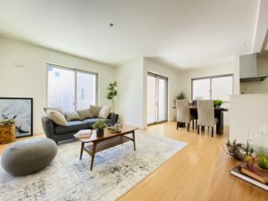 A bright and spacious living and dining room with modern furniture, wooden flooring, and natural light streaming through large windows.